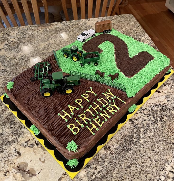 a birthday cake that is on top of a table with cars and farm equipment in the background