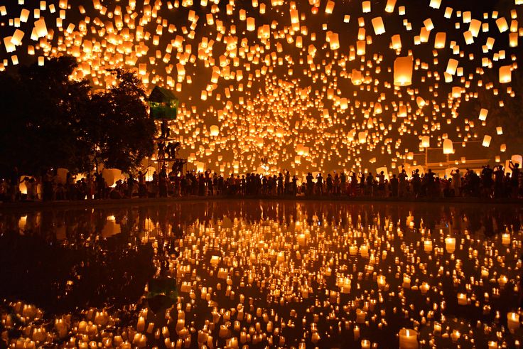 many lit up lanterns floating in the air over water at night with reflections on the ground