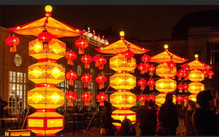 many red and yellow lanterns are hanging from the ceiling in front of a building at night