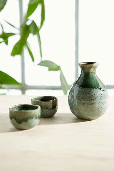 three green vases sitting on top of a wooden table next to two empty bowls