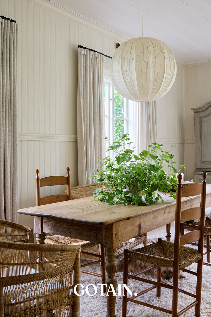 a dining room table with chairs and plants on it in front of a window that has white paneling