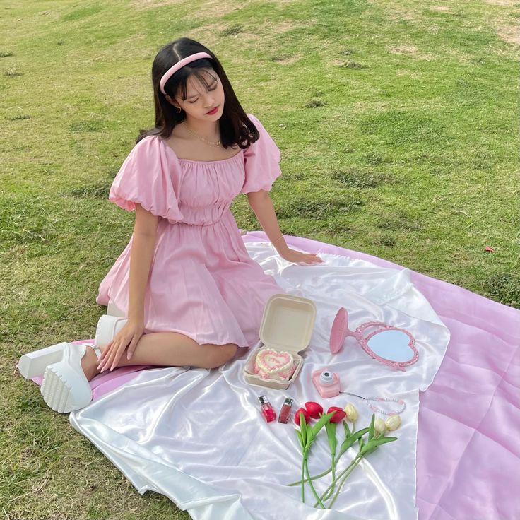 a young woman sitting on top of a pink blanket next to a cake and flowers