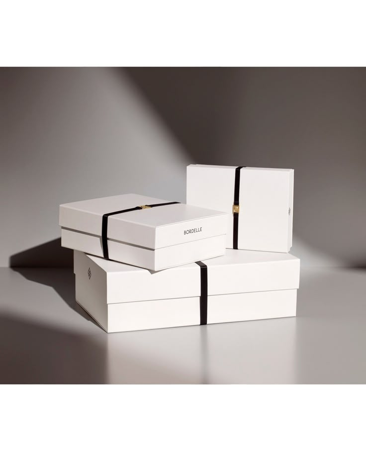 three white boxes with black ribbons on them sitting next to each other in front of a gray background