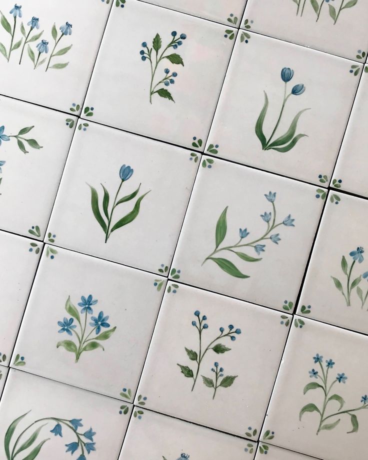 blue flowers and green leaves are painted on white tiles in this tile design that is part of a wall