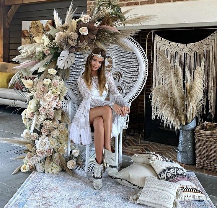 a woman sitting in a white chair next to a fire place with flowers on it