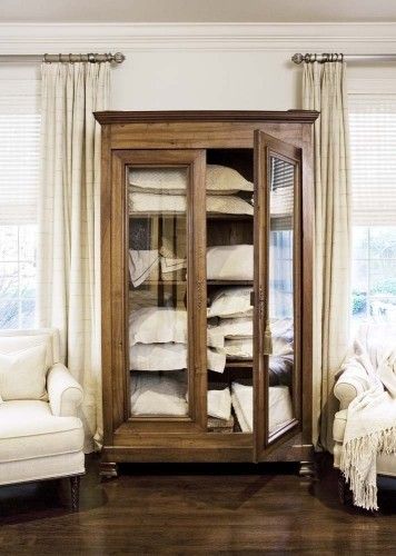 a wooden cabinet filled with lots of white linens in a living room next to a chair