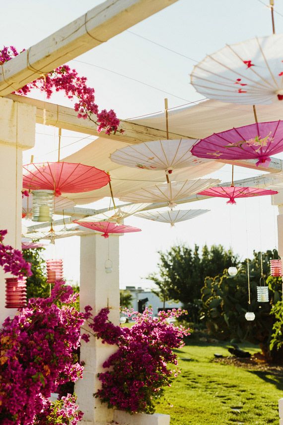 many umbrellas are hanging from the ceiling over some plants and flowers in front of a house