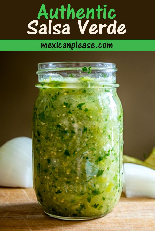 a jar filled with green salsa sitting on top of a wooden table next to onions