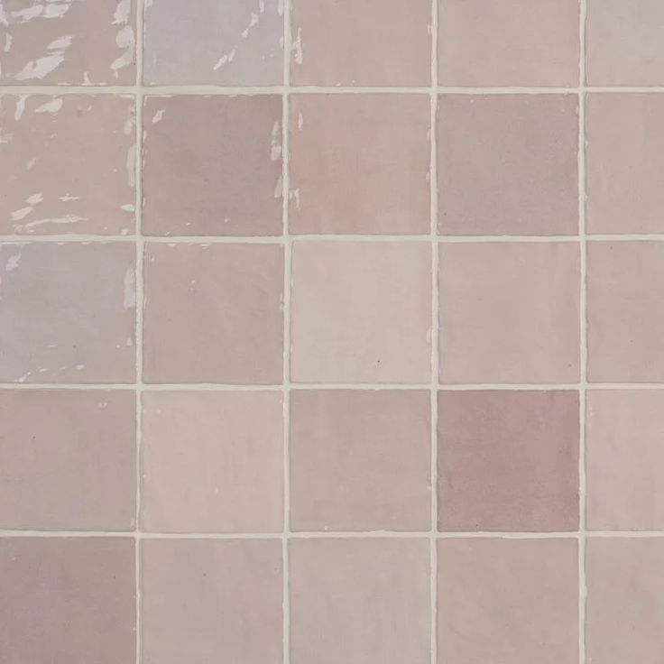 a white toilet sitting in front of a tiled wall with pink and grey tiles on it