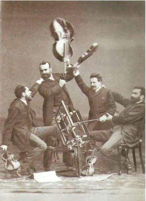 an old photo of men sitting around a motorcyclist with his arms in the air