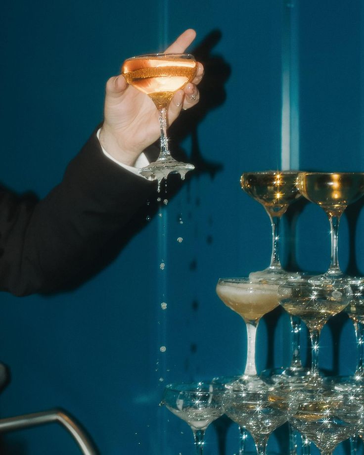 a man in a tuxedo holding up a wine glass next to several champagne goblets