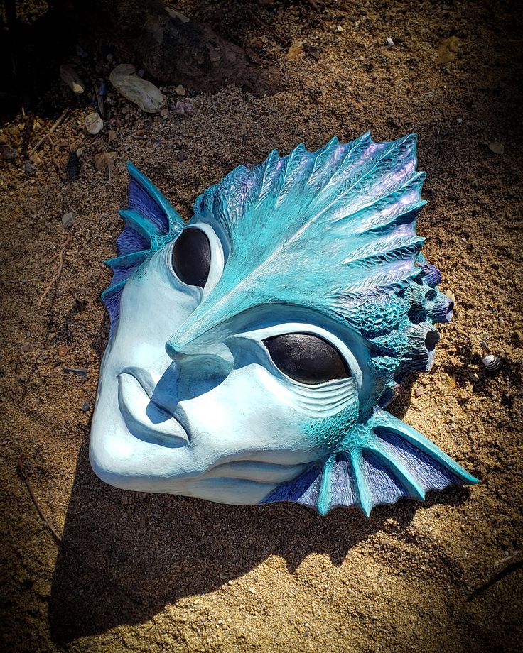 a blue and white mask laying in the sand with its eyes open, on top of dirt