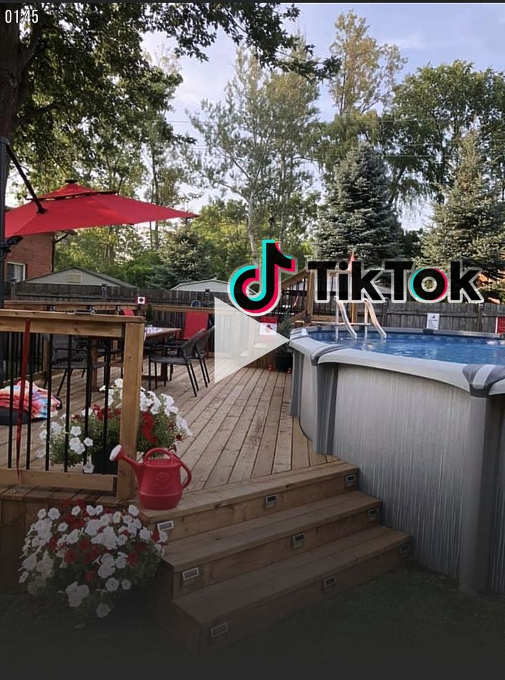 an above ground swimming pool with decking and umbrellas in the background, surrounded by flowers