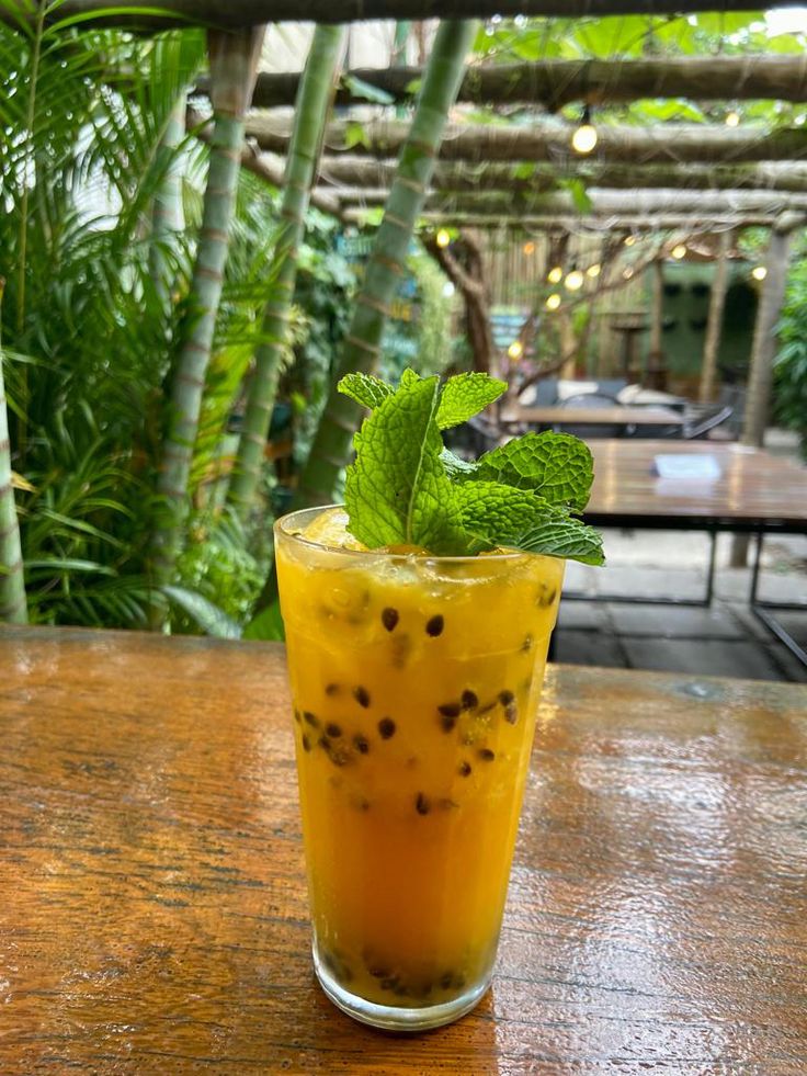 a tall glass filled with orange juice and green leafy garnish on top of a wooden table