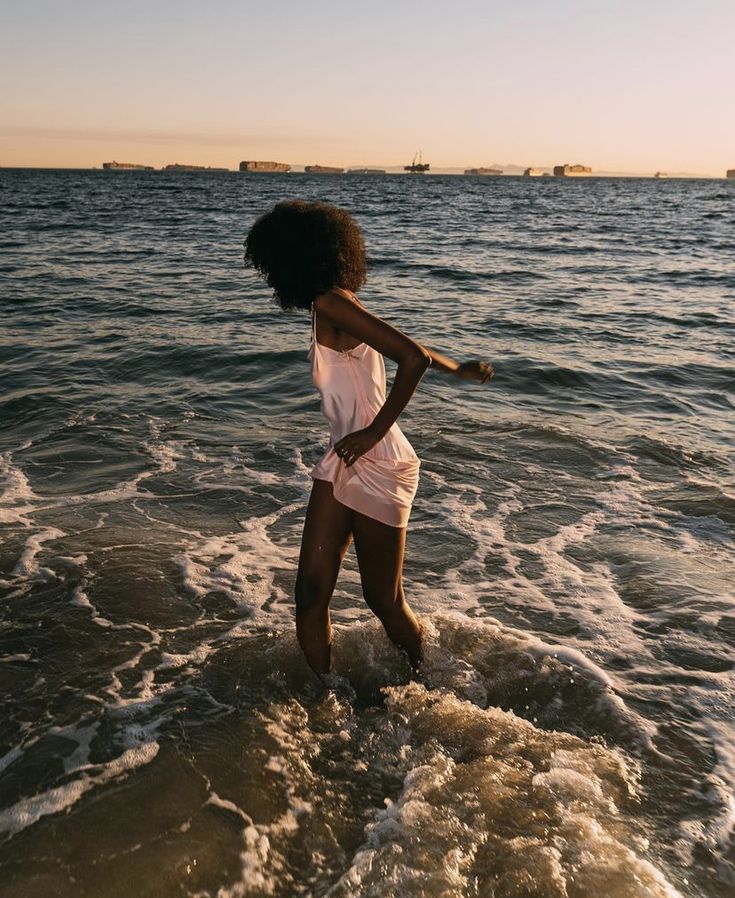 a woman standing in the water on top of a beach