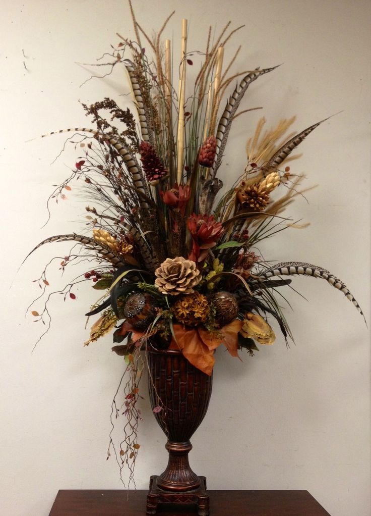 a vase filled with lots of dried flowers on top of a wooden table next to a wall