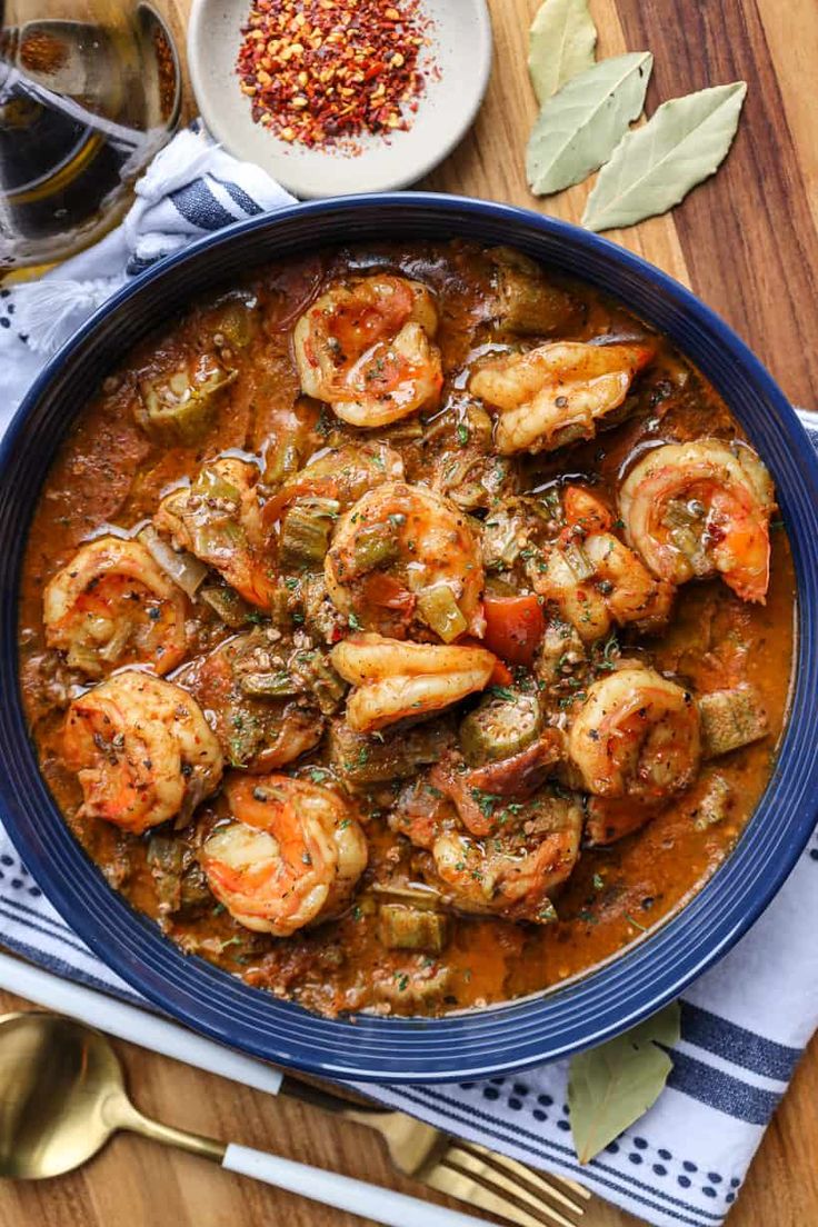 a blue bowl filled with shrimp and tomato stew on top of a wooden cutting board