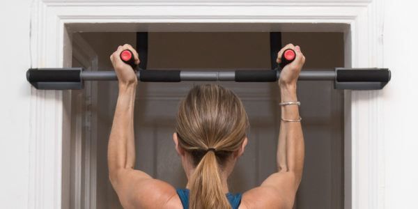 a woman doing pull ups on a bar in front of a white door with black handles