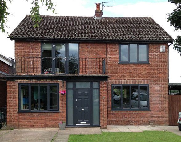 a large brick house with black doors and windows on the front lawn, next to a car