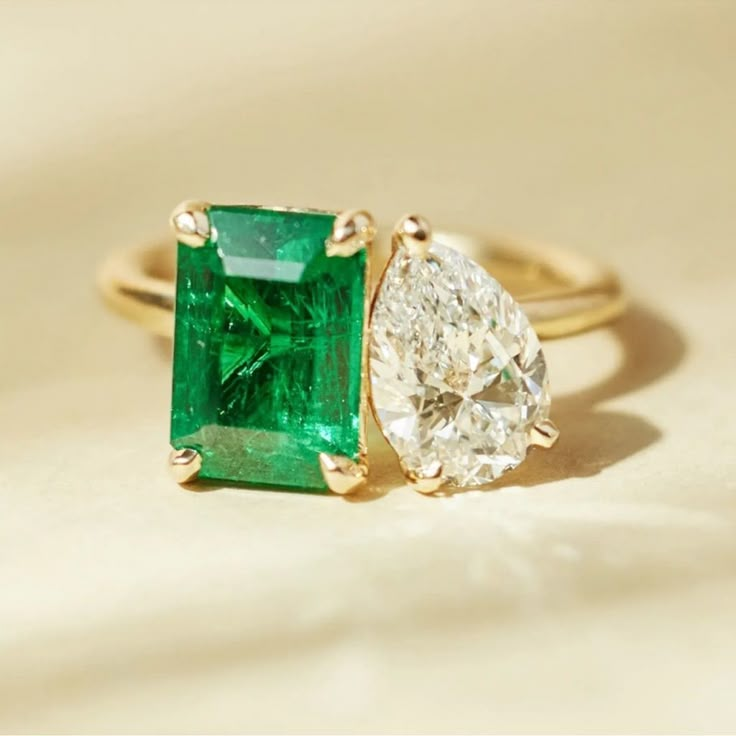 an emerald and diamond ring sitting on top of a white cloth covered table with gold trimming