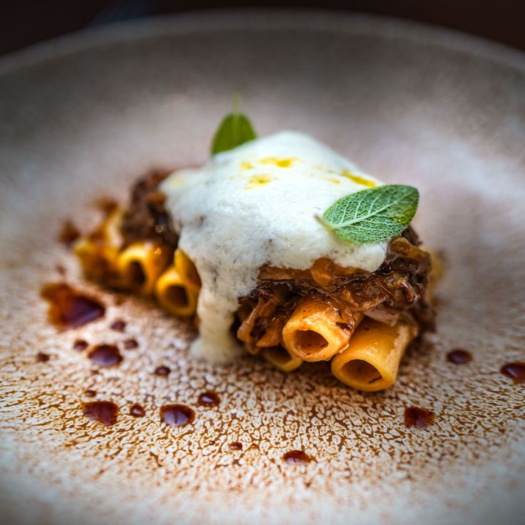 a white plate topped with lasagna covered in sauce and cheese, garnished with green leaves