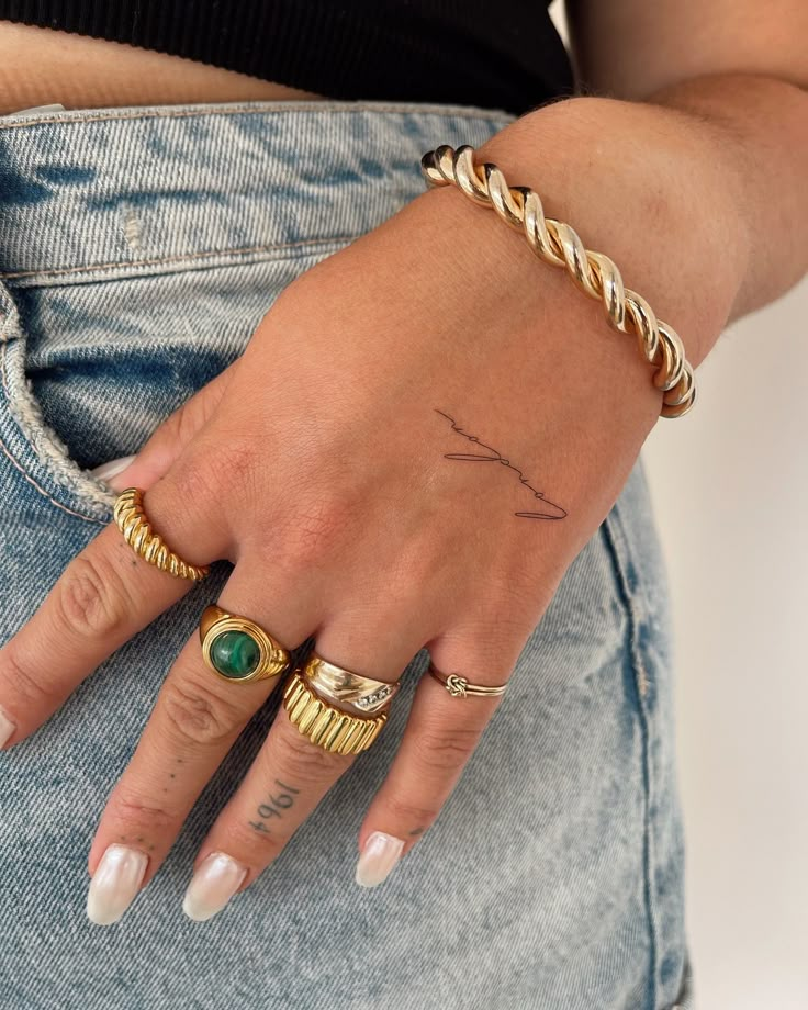 a woman's hand with two gold rings on her left and one green ring on her right