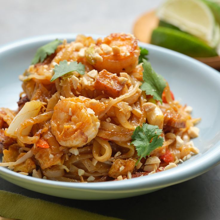 a white plate topped with noodles and vegetables next to lime wedges on a table