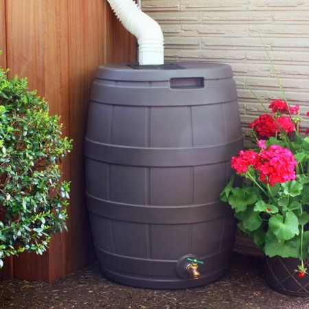 a large black barrel sitting next to some potted plants on the side of a building