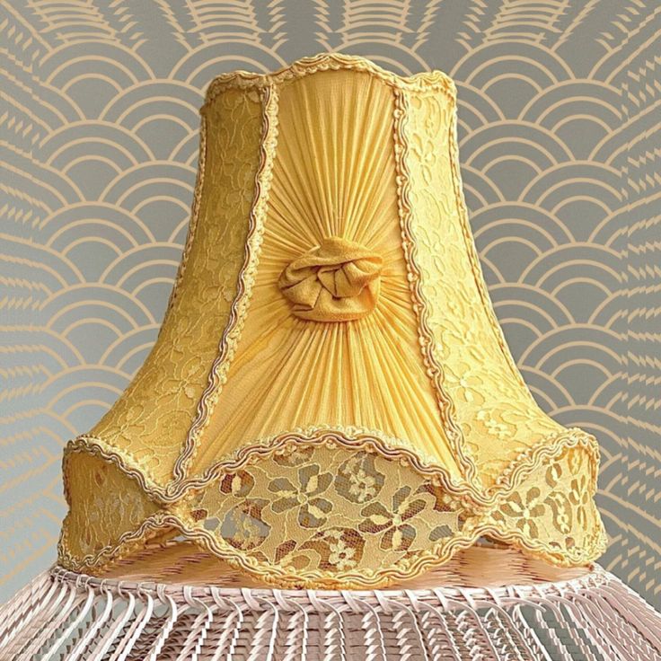 a yellow lamp shade sitting on top of a table next to a wallpapered background