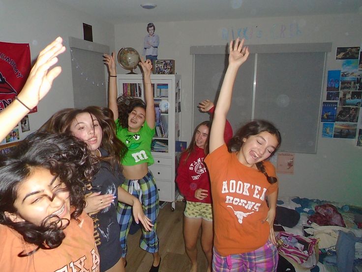 a group of young women standing around each other in a living room with their arms up