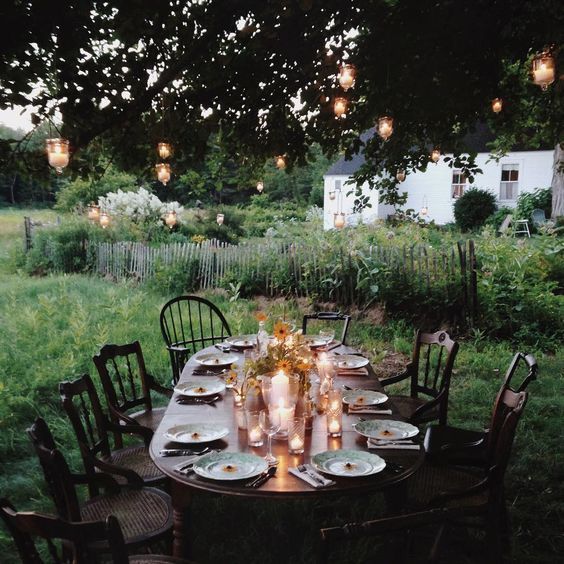 an outdoor dinner table set up with candles and plates in the grass, surrounded by trees