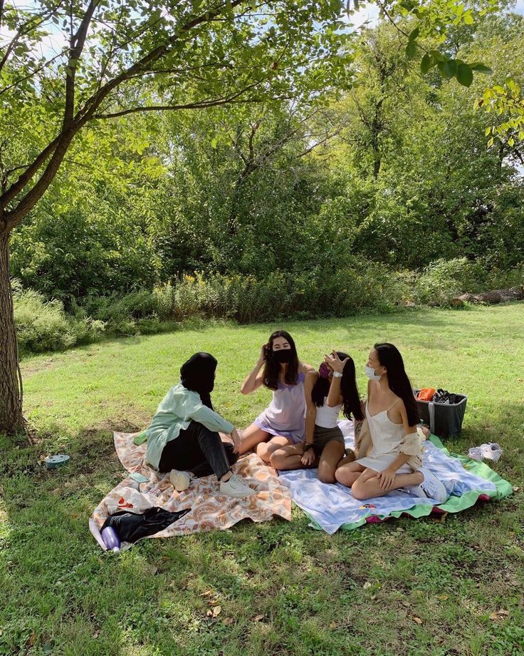 three women sitting on a blanket in the grass and one woman is taking pictures with her phone