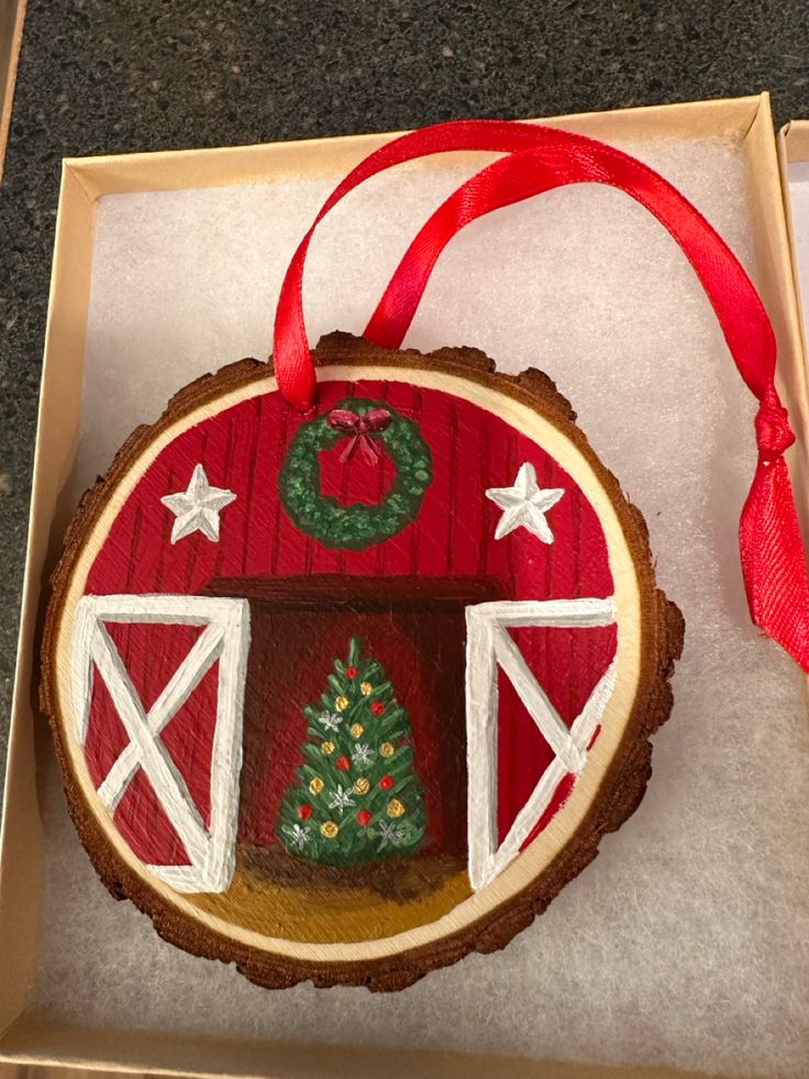 a christmas ornament in a box with a red ribbon and tree on it