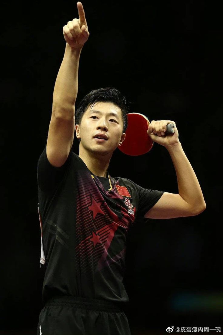 a man holding a ping pong paddle in his right hand and giving the peace sign