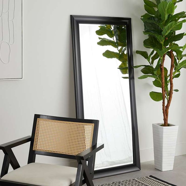 a black framed mirror sitting next to a chair and potted plant