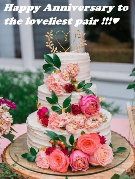 a wedding cake with pink flowers and greenery on the top is sitting on a tree stump