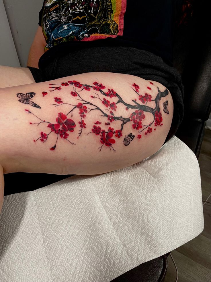 a woman's arm with red flowers and butterflies on it, while sitting in a chair