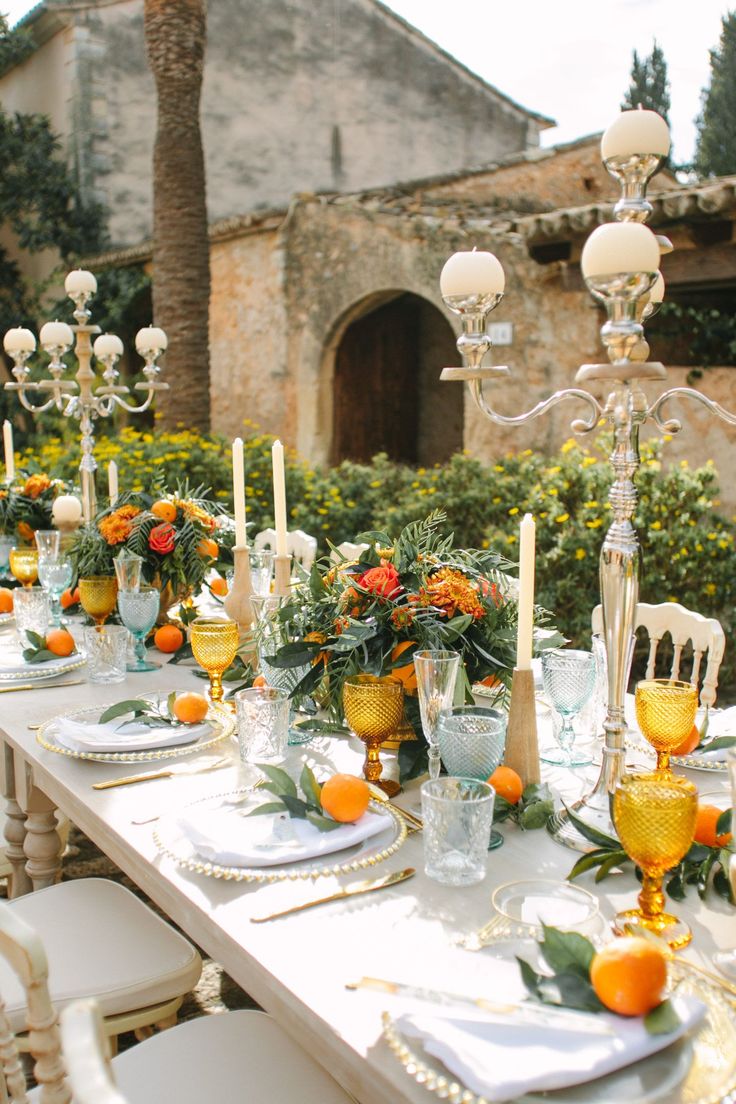 an outdoor dining table set with oranges and white place settings for two people to sit at