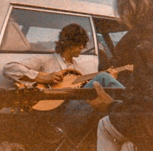 two men are playing guitars in front of a car