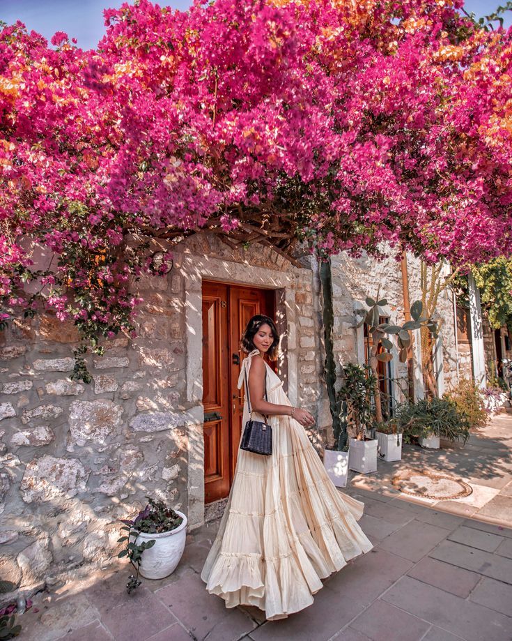 a woman standing in front of a doorway with pink flowers on the wall and potted plants