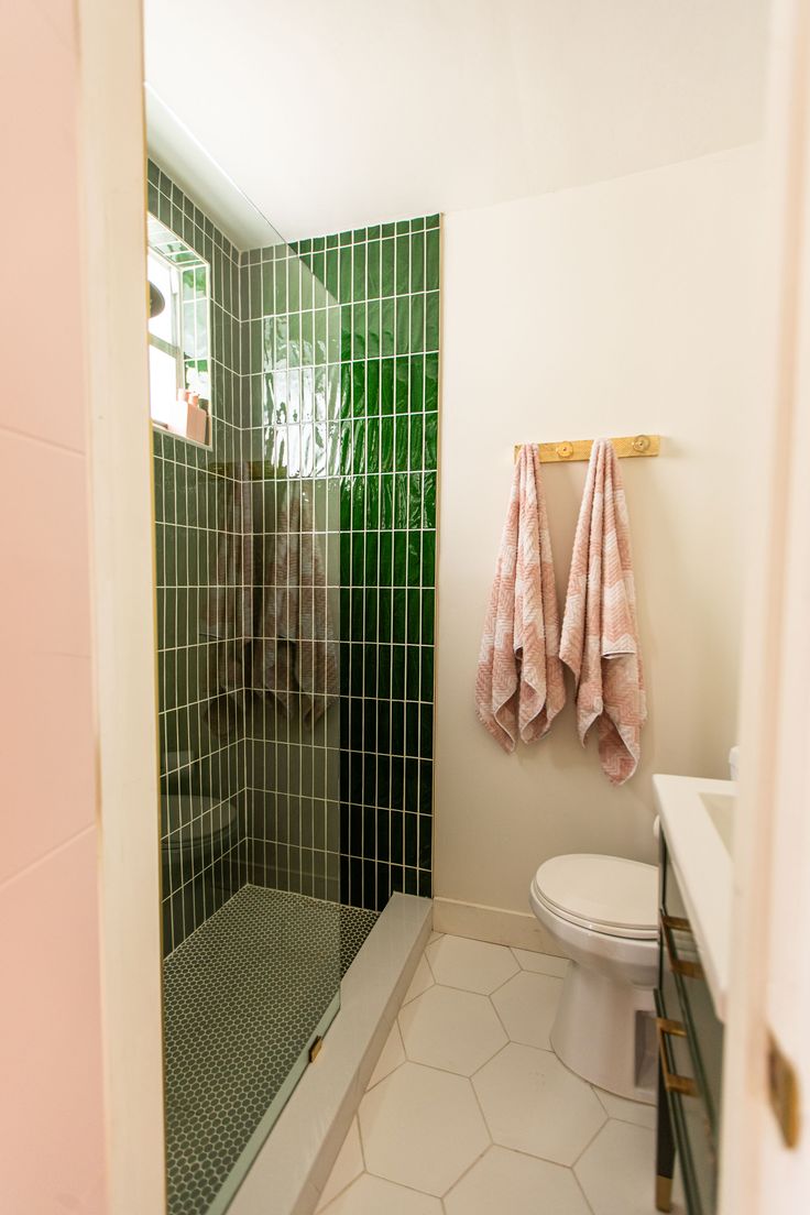 a green tiled bathroom with two towels hanging on the wall