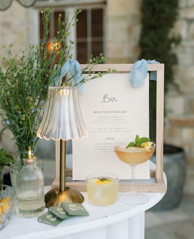 a table topped with drinks next to a lamp and vases filled with flowers on top of a white table