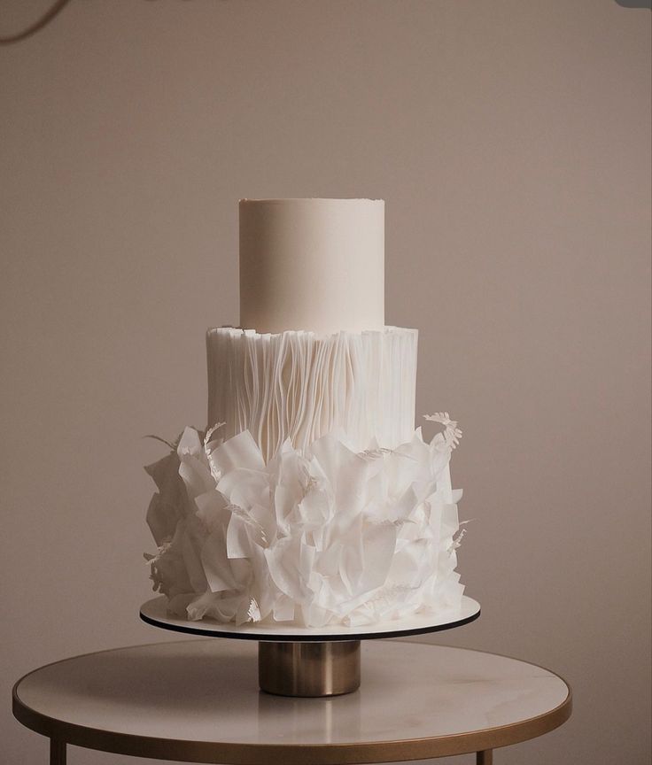 a three tiered white wedding cake with ruffles