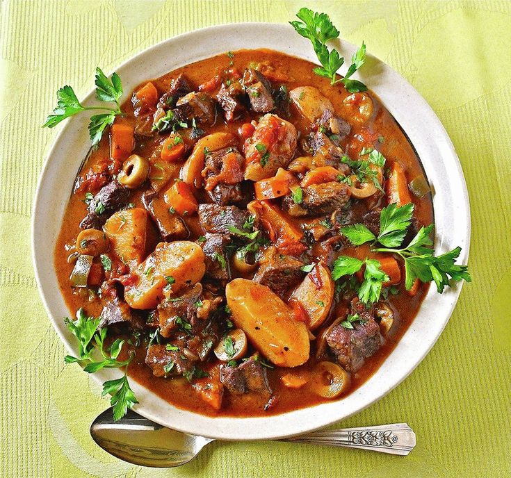 a white bowl filled with stew on top of a green table cloth next to a spoon