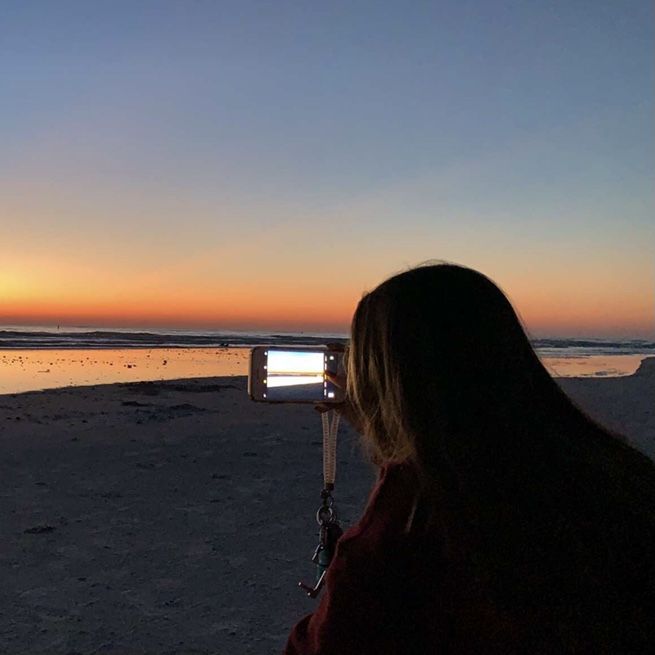 a woman taking a photo on the beach at sunset