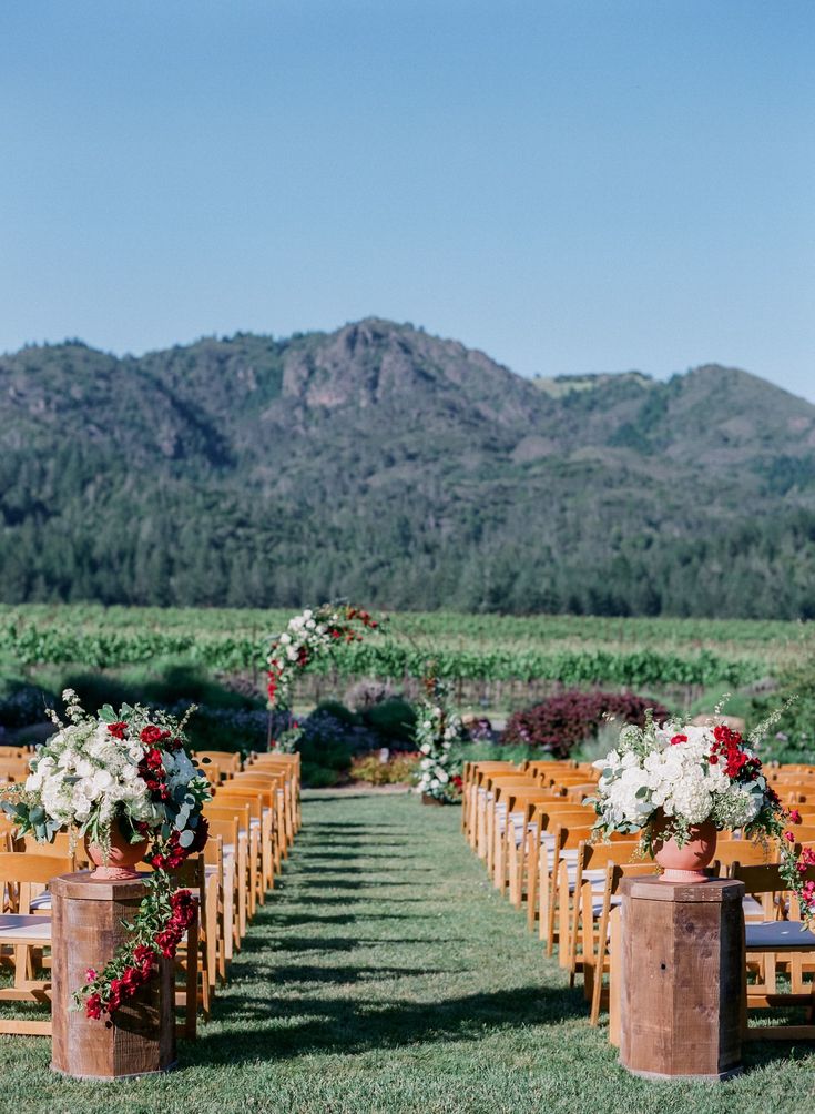 an outdoor ceremony setup with wooden chairs and flowers in vases on each side of the aisle