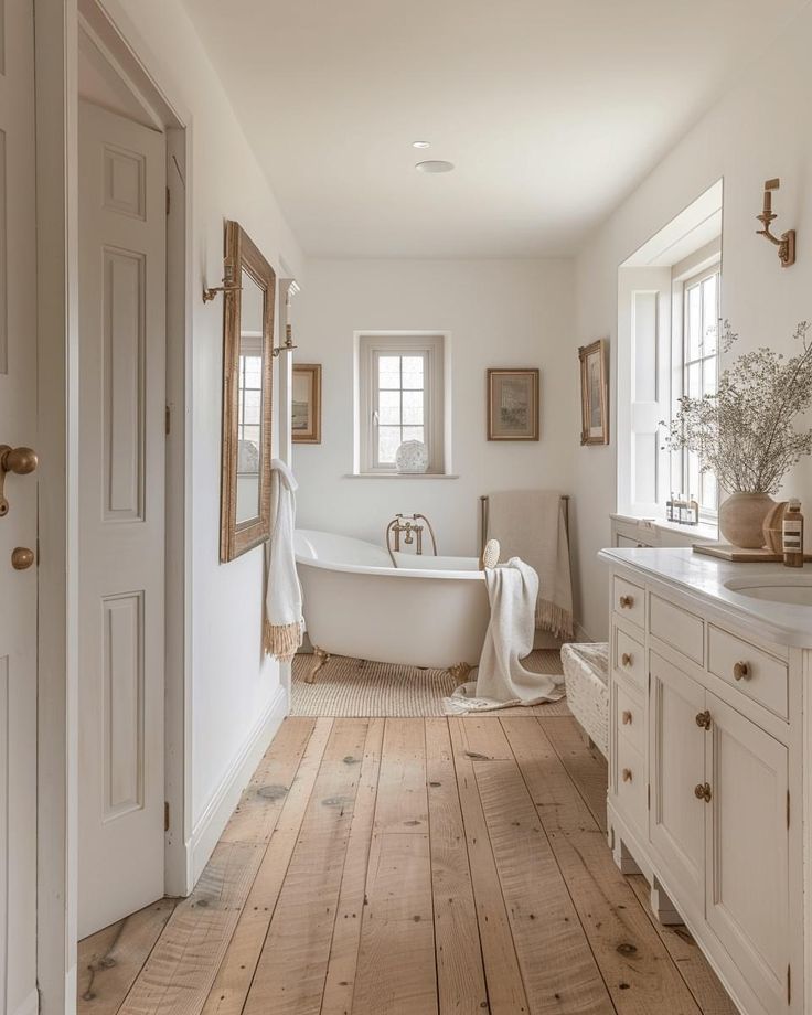 a white bathroom with wooden floors and an antique bathtub in the corner, along with two windows