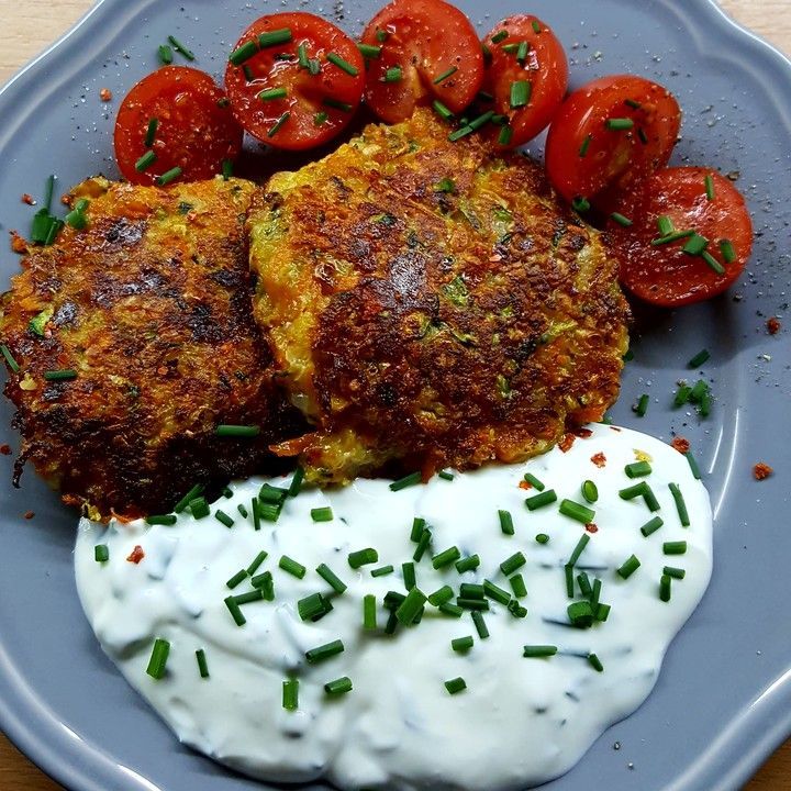 two crab cakes on a plate with sour cream and tomatoes