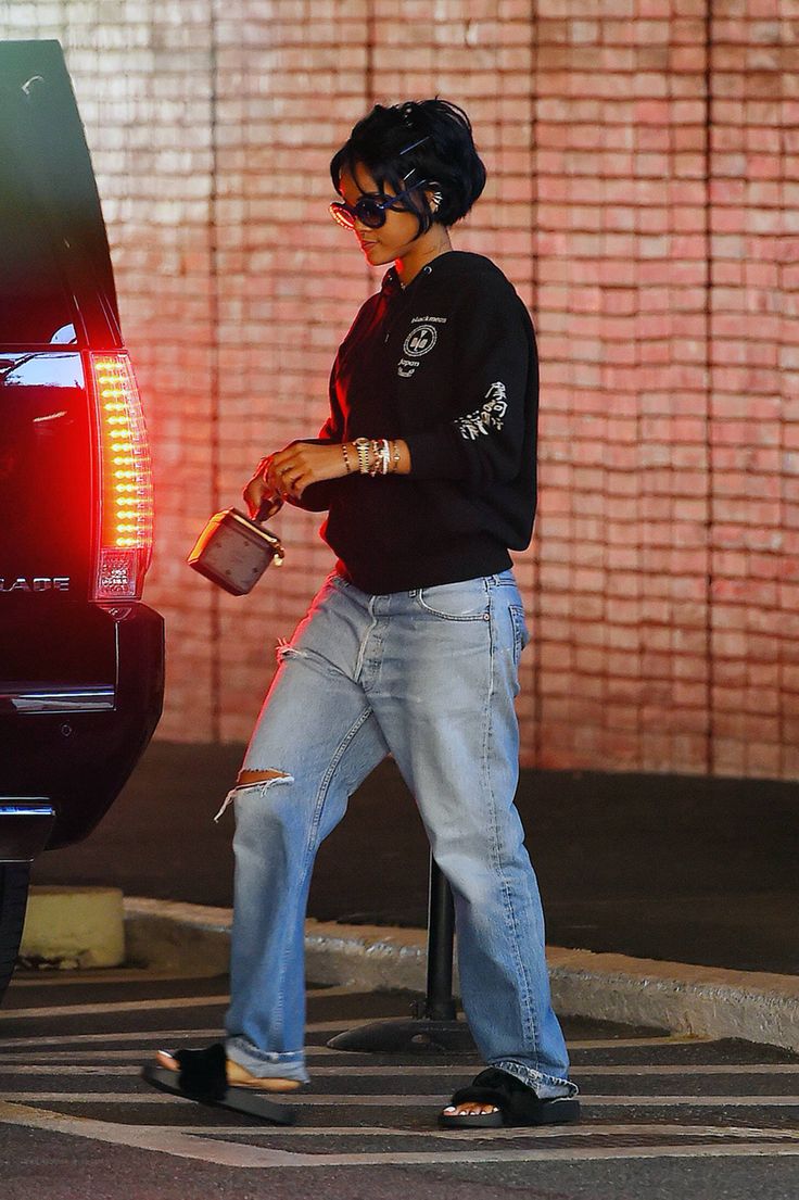 a woman in black shirt and jeans standing next to a car