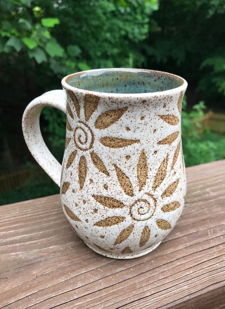 a white and brown coffee cup sitting on top of a wooden table next to trees